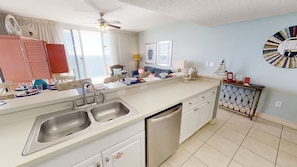 A modern kitchen with a double sink, a dishwasher, and a dining area with a table set for two.