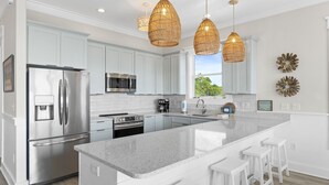 A modern kitchen with white cabinets, stainless steel appliances, a granite countertop, and wicker pendant lights.