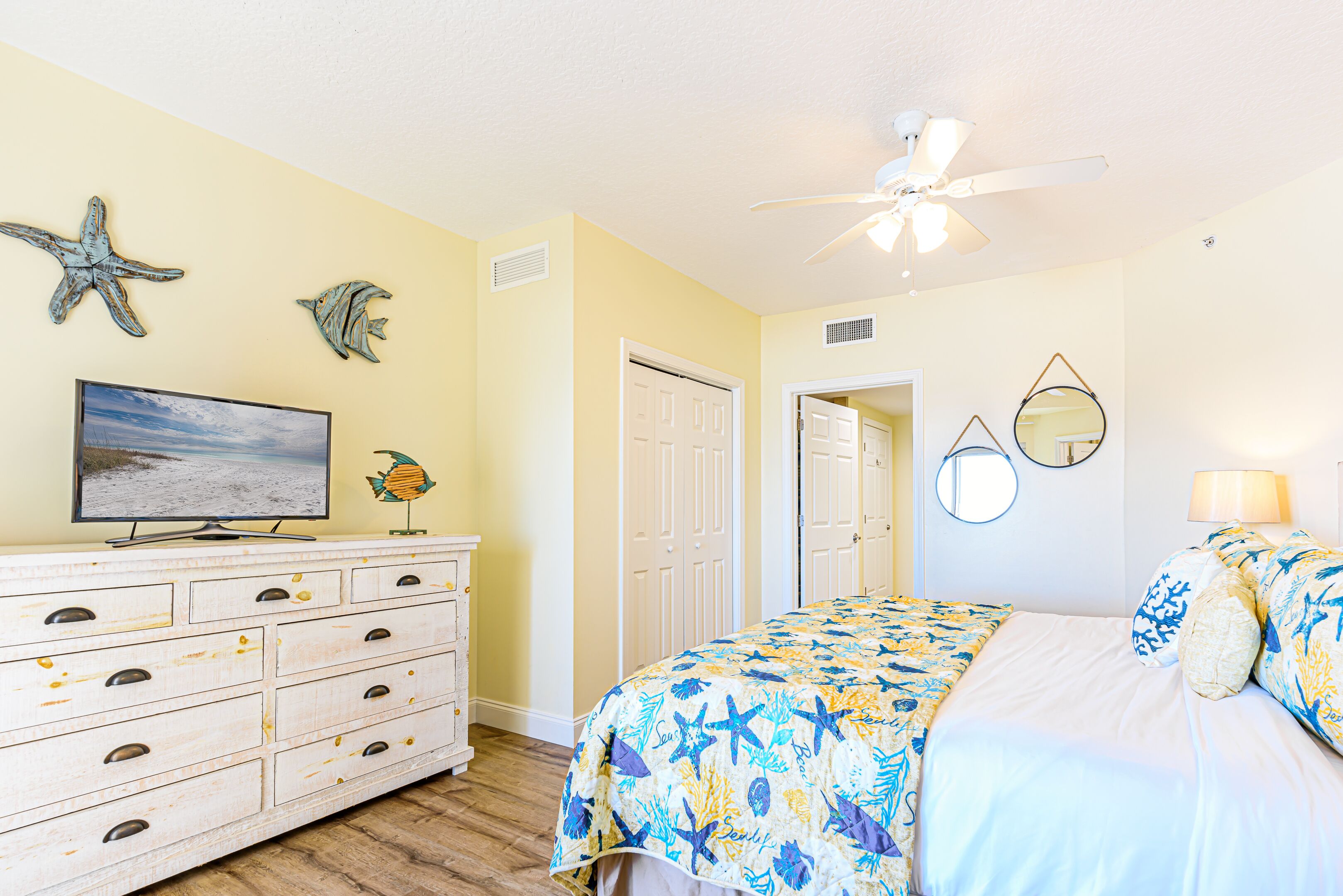 A bedroom with a bed, dresser, television, and decorative wall art.