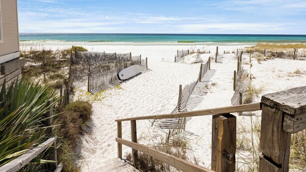A beach view with a wooden fence, a white surfboard, and a sandy path leading to the ocean. - Gulf Front - Beach Chairs - Seagrove Beach! (Santa Rosa Beach)