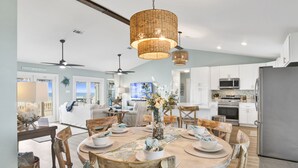 A spacious kitchen with white cabinets, a stainless steel refrigerator, and a dining area with a wooden table and chairs. - Beachfront | Pet Friendly | Renovated Coastal Cottage (Gulf Shores)