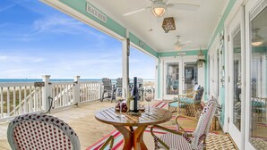 A covered outdoor area with a table and chairs, a view of the beach, and a sign reading "Beach House". - Beachfront | Pet Friendly | Renovated Coastal Cottage (Gulf Shores)