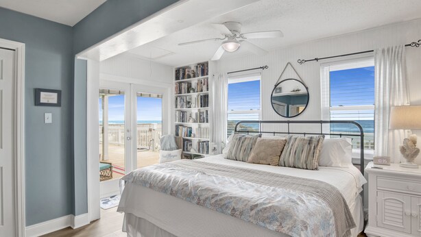 A bedroom with a bed, a ceiling fan, a bookshelf, and a view of the ocean. - Beachfront | Pet Friendly | Renovated Coastal Cottage (Gulf Shores)