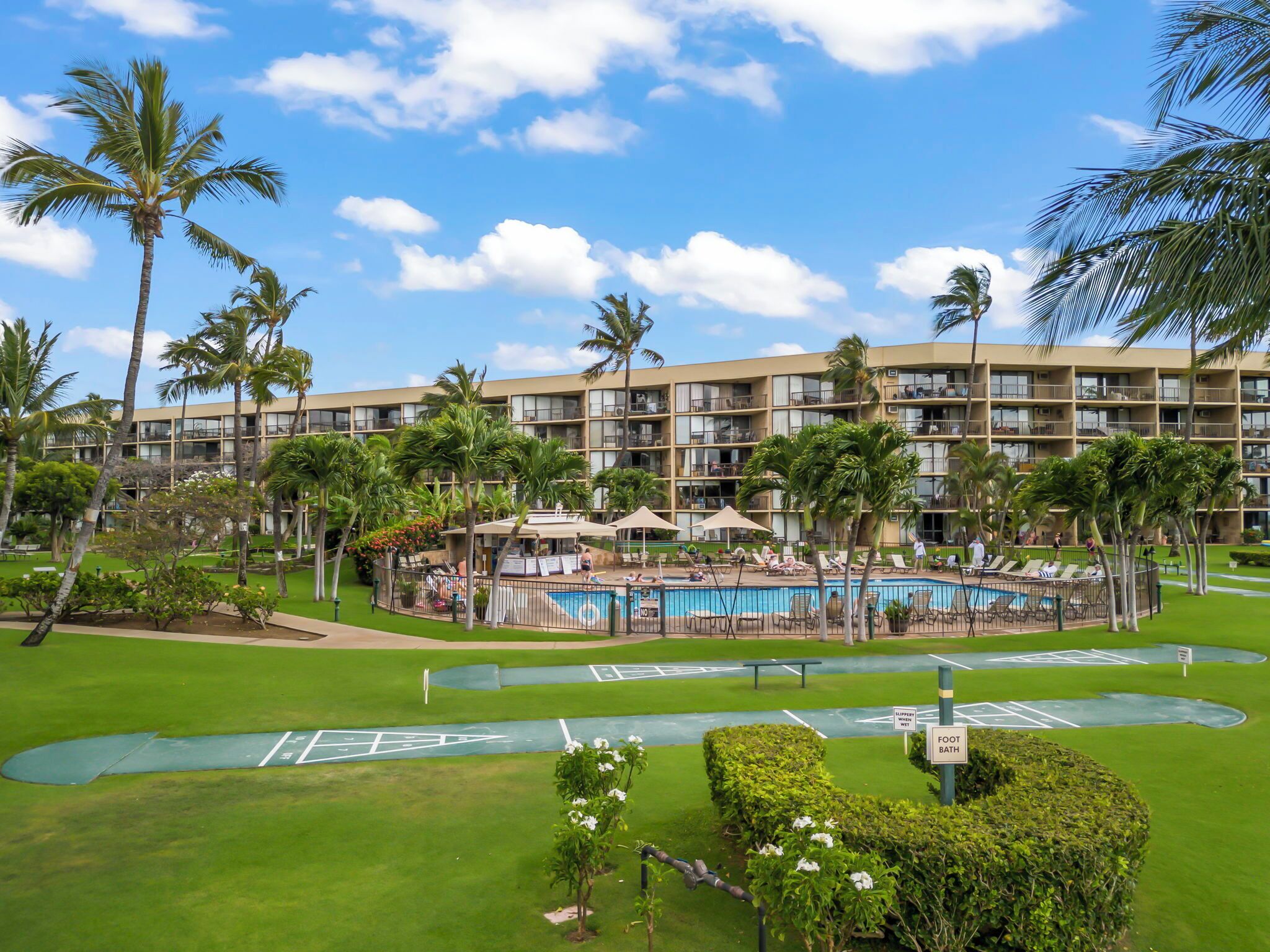 A resort with a swimming pool, palm trees, and a multi-story building with balconies.
