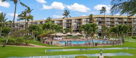 A resort with a swimming pool, palm trees, and a multi-story building with balconies.