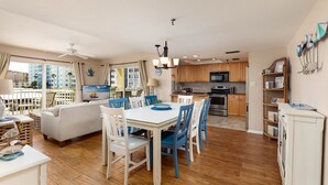 A spacious living area with a dining table, chairs, a sofa, and a kitchen with wooden cabinets and appliances. - Heated Pool/Spa - Beachside! , Sleeps 10, Balcony 101 (Redington Shores)