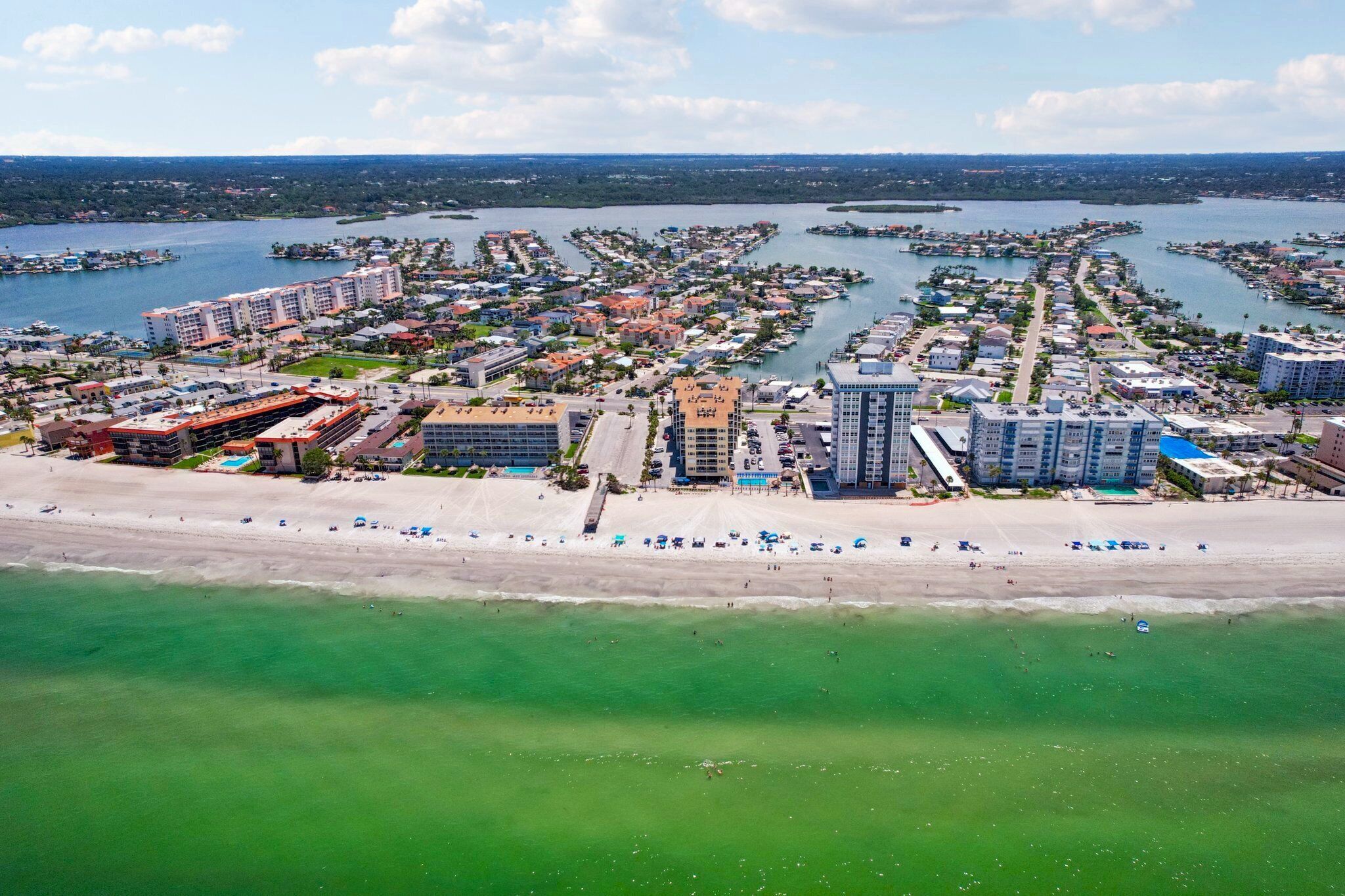 Een kuststree uitzicht met een strand, jachthaven en woongebouwen.