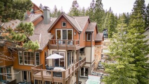 A two-story wooden house with a balcony, outdoor seating, and a hot tub.