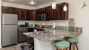 A modern kitchen with dark wood cabinets, stainless steel appliances, a granite countertop, and pendant lighting. - Beachfront Condo | Stunning Views, Private Balconies & Pool (Corpus Christi)
