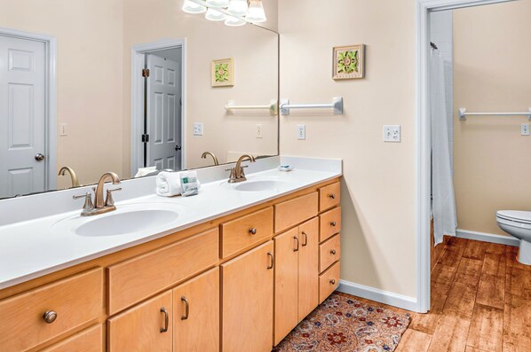 A bathroom with a large mirror, two sinks, wooden cabinets, a towel rack, and a wooden floor.