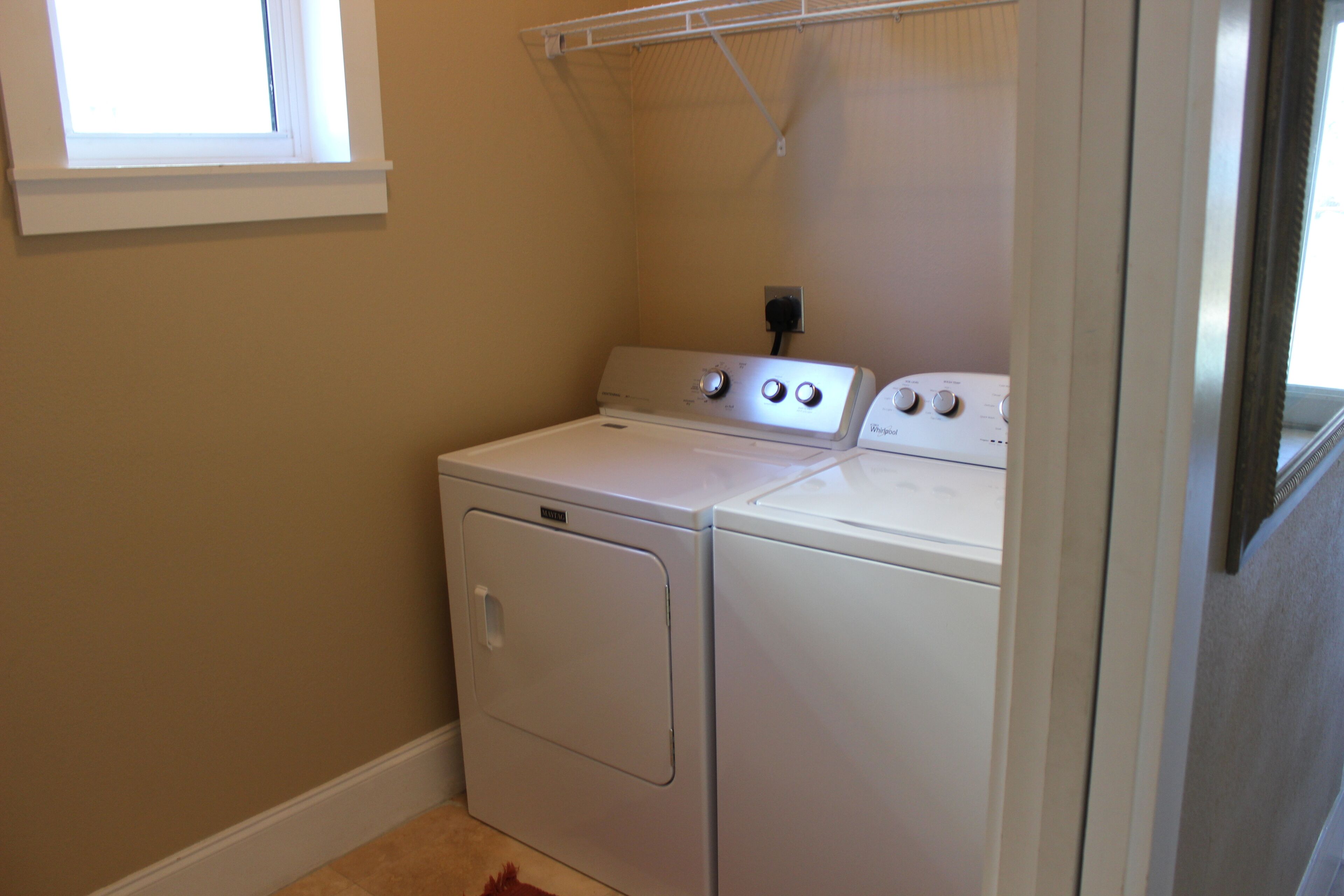 A laundry room with two white washers and dryers, a window, and a metal shelf above the dryers.