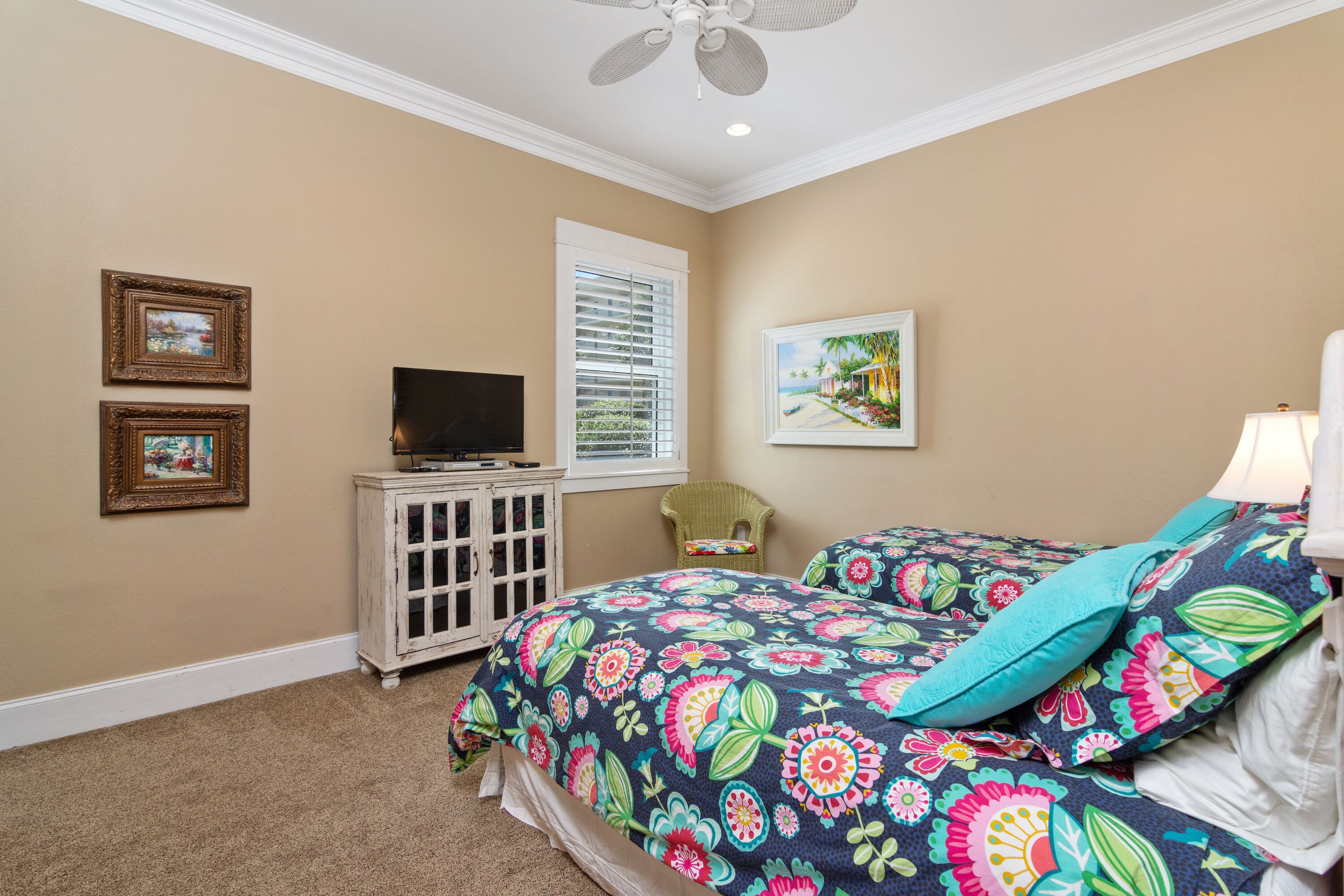 A bedroom with a bed, a TV on a cabinet, a window with blinds, and two framed pictures on the wall.