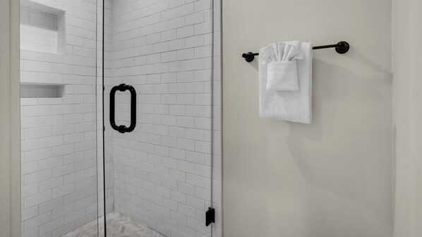 Een badkamer met witte betegeling, een zwarte handdoekhouder en een witte handdoek aan de muur.