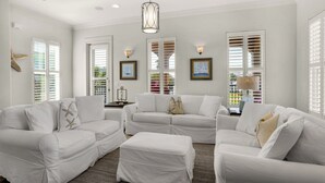 A spacious living room with white furniture, large windows with shutters, and artwork on the walls. - Private Pool & Beach Access + Free Tickets: Bikes, Dolphin Cruise & More! (Seacrest)