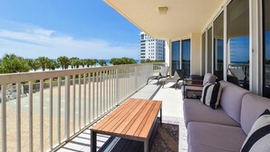 Uma varanda com uma mesa de madeira, um sofá e vista para o mar e edifícios.