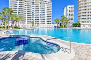 A swimming pool with a hot tub, surrounded by palm trees and modern high-rise buildings. - Colorful, bright beachfront condo w/private balcony! ☀️ (Destin)