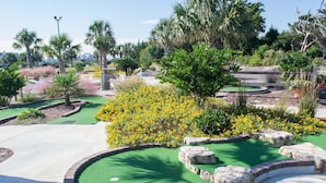Un terrain de golf bien entretenu, doté d’un green d’entraînement, entouré d’une végétation luxuriante et de plantes en fleurs.