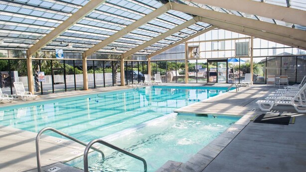 Une piscine couverte à l’eau claire, entourée de chaises longues et dotée d’une structure de toit en verre.