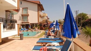 Une zone avec une piscine, des chaises longues et des parasols, un bâtiment sur lequel on peut lire l’inscription « SAF », et un ciel dégagé.