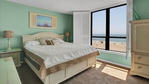 Une chambre à coucher comprenant un lit, une table de chevet, une commode et une fenêtre donnant sur la plage.