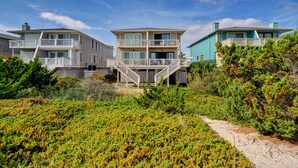 Una propiedad frente a la playa con una casa de varios niveles, balcones y una escalera que conduce a la entrada.
