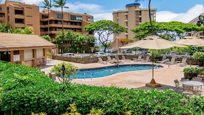 A resort pool area with lounge chairs, umbrellas, and a view of surrounding buildings. - Loft living in a Spacious, remodeled 2bd Condo (Lahaina)