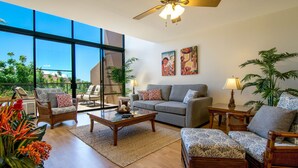 A spacious living room with a large window, a ceiling fan, and a sofa set. - Loft living in a Spacious, remodeled 2bd Condo (Lahaina)