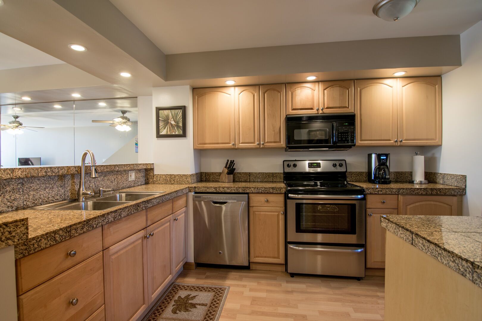 A modern kitchen with granite countertops, stainless steel appliances, wooden cabinets, and a ceiling fan.
