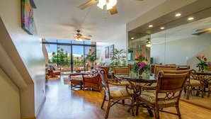 A spacious living area with a large glass wall, wooden furniture, and ceiling fans. - Loft living in a Spacious, remodeled 2bd Condo (Lahaina)