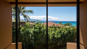 A view from a balcony with a clear sky, palm trees, and a distant ocean. - Loft living in a Spacious, remodeled 2bd Condo (Lahaina)