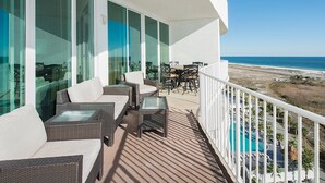 Uma varanda com mobiliário de vime, grandes janelas e vista para a praia e o oceano.