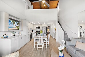 A spacious kitchen with white cabinets, a dining area with a wooden table and chairs, and a staircase leading to an upper level. - Grand 3bd ocean view condo at pristine resort (Lahaina)