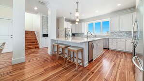 A spacious kitchen with a large island, wooden bar stools, and a view to the outside. - Endless Summer by GSVR | 7BR Beachfront Home w/ Pool & Handicap Access + FREE Activities/Golf (Gulf Shores)