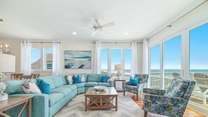 A spacious living room with a large sectional sofa, a coffee table, and a patterned rug. There are large windows offering a view of the ocean. - Endless Summer by GSVR | 7BR Beachfront Home w/ Pool & Handicap Access + FREE Activities/Golf (Gulf Shores)