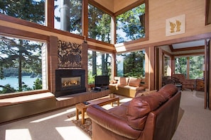Un salón amplio con chimenea, asientos cómodos y ventanas grandes que ofrecen vistas al exterior.