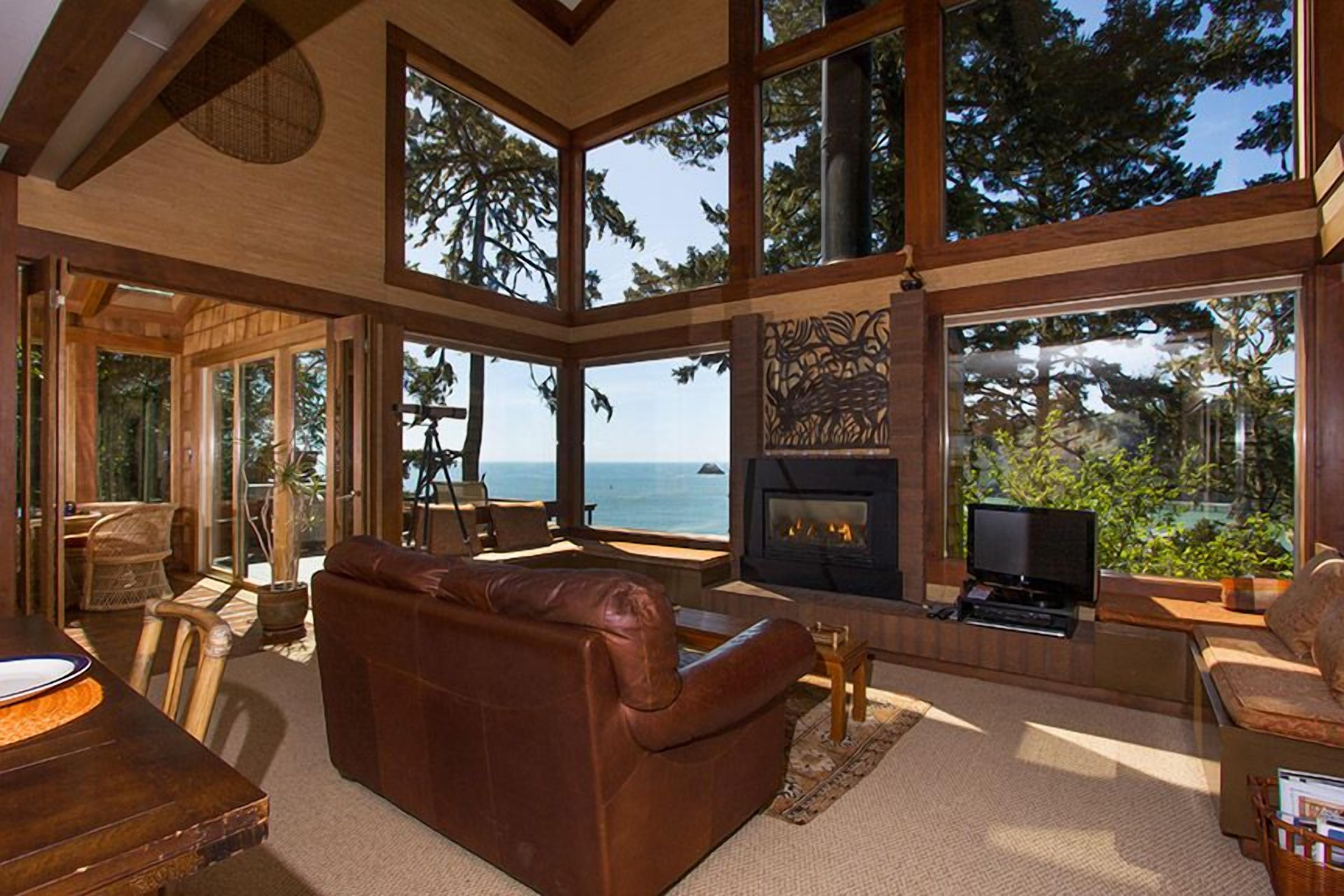 Een ruime woonkamer met een open haard, grote ramen en uitzicht op de oceaan.