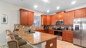 Una cucina moderna con piani in granito, mobili in legno, elettrodomestici in acciaio inossidabile e un'isola integrata con posti a sedere al bancone.