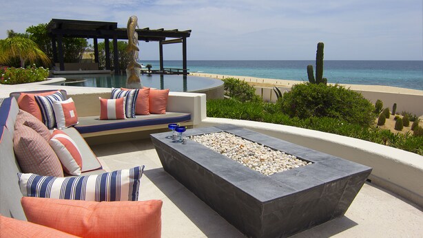 A poolside seating area with a fire pit, overlooking a beach and ocean.