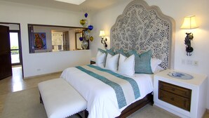 A bedroom with a large bed, a bedside table, a nightstand, a mirror, and decorative wall art.