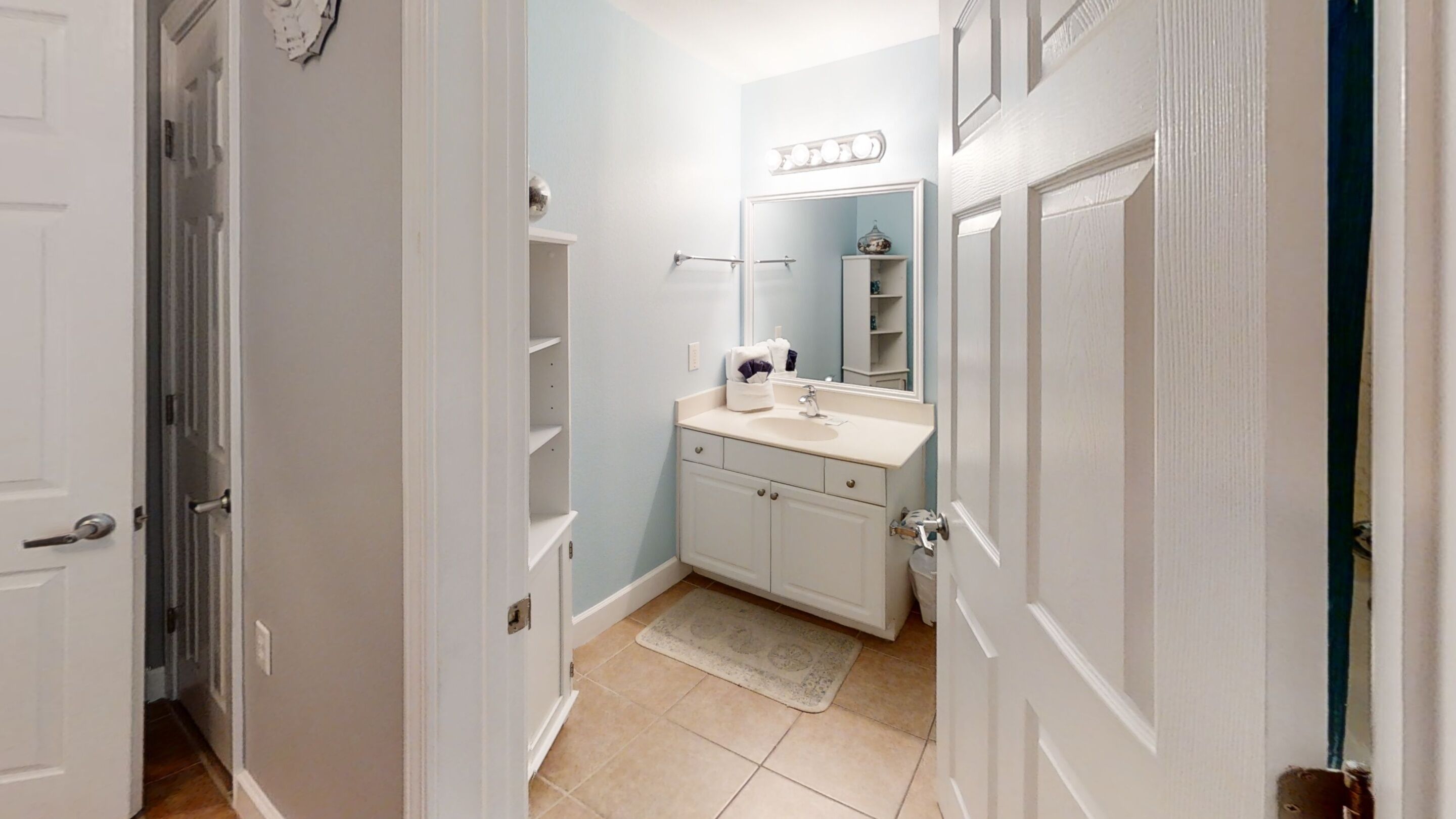 A narrow hallway leading to a bathroom with a sink, mirror, and shelves.