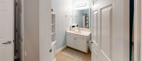 A narrow hallway leading to a bathroom with a sink, mirror, and shelves.