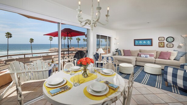 A dining area with a table set for four, overlooking a beach with palm trees and the ocean. - Panoramic Ocean View White Sandy Beaches   Community Jacuzzi (Oceanside)