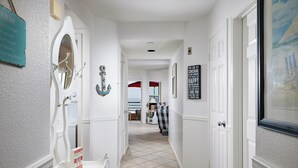 A hallway with white walls, a tiled floor, and nautical-themed decorations including an anchor and a sign with nautical words. - Panoramic Ocean View White Sandy Beaches   Community Jacuzzi (Oceanside)