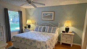 A bedroom with a bed, two bedside tables with lamps, a ceiling fan, a window with curtains, and a framed picture on the wall. - Chic Gem in The Villages - Modern Amenities & Prime Location! Call today! (The Villages)