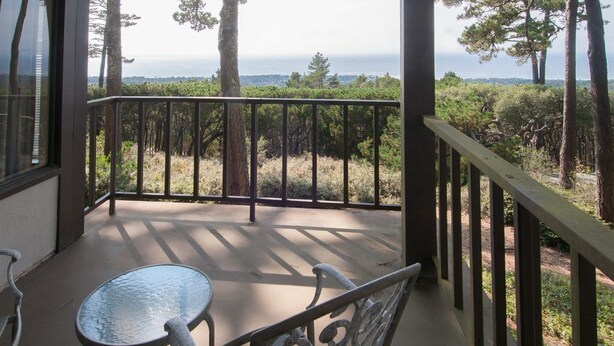 A covered outdoor area with a table and chairs, overlooking a forested landscape and the ocean. - Ocean Pines #28 - Pebble Beach Condo - Oceanview Luxury (Pebble Beach)