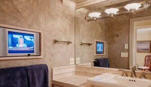 A bathroom with a large mirror, a television mounted on the wall, and a sink with a towel rack.