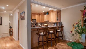 A kitchen with wooden cabinets, a marble countertop, and bar stools. - Ocean Pines #28 - Pebble Beach Condo - Oceanview Luxury (Pebble Beach)