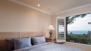 A bedroom with a bed, a nightstand, a lamp, and a window with blinds. - Ocean Pines #28 - Pebble Beach Condo - Oceanview Luxury (Pebble Beach)