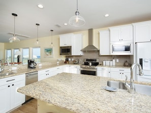 A modern kitchen with white cabinets, granite countertops, stainless steel appliances, and pendant lighting.