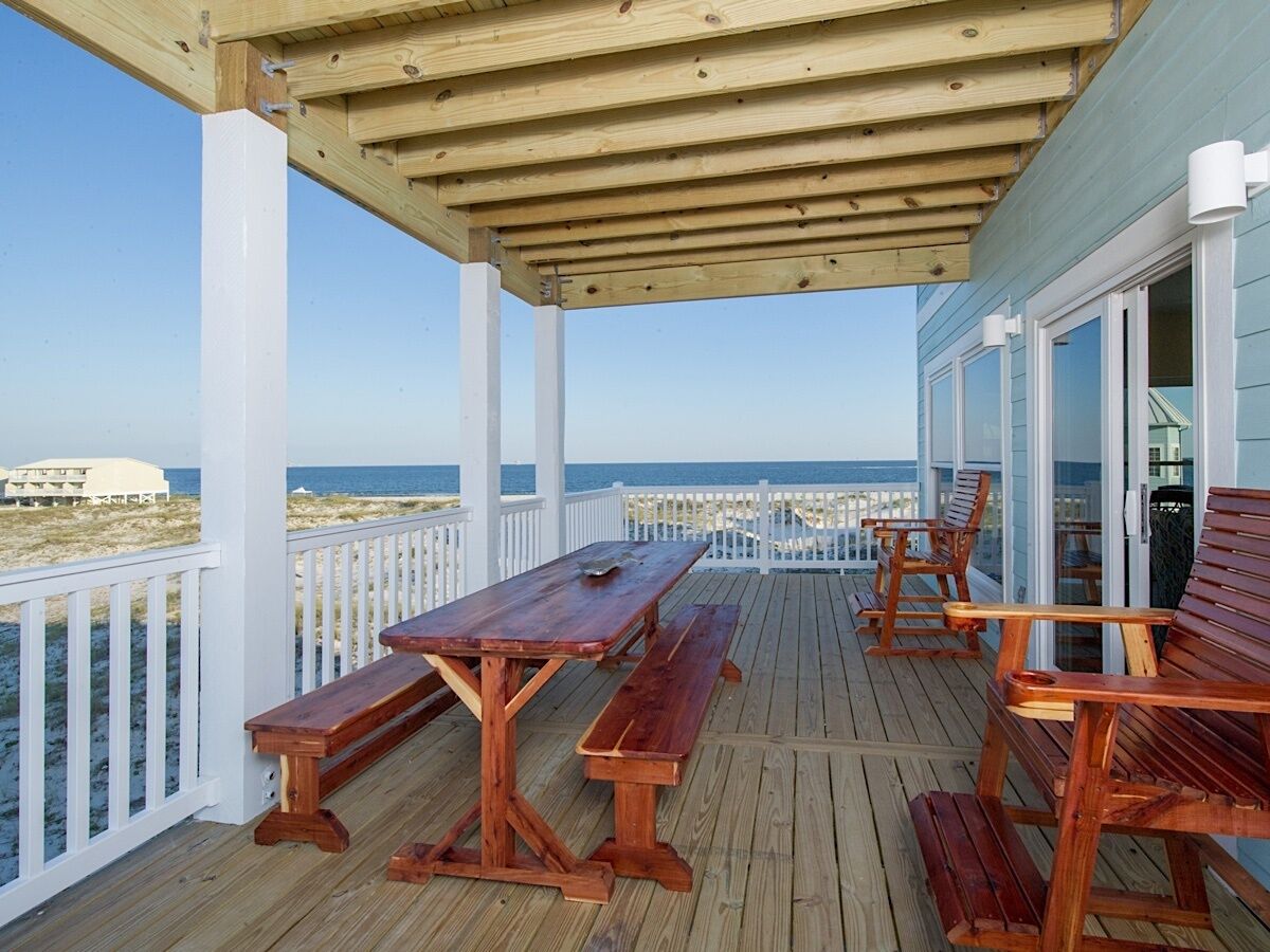 A wooden deck with a table and benches, overlooking the beach and ocean.